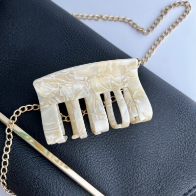 Plaukų segtukas žnyplės, kurio paviršius atrodo lyg išlieto balto šokolado. Segtukas ant juodos delninukės