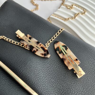 Tigrinių raštų makiažo plaukų segtukai padėti ant juodos delninukės