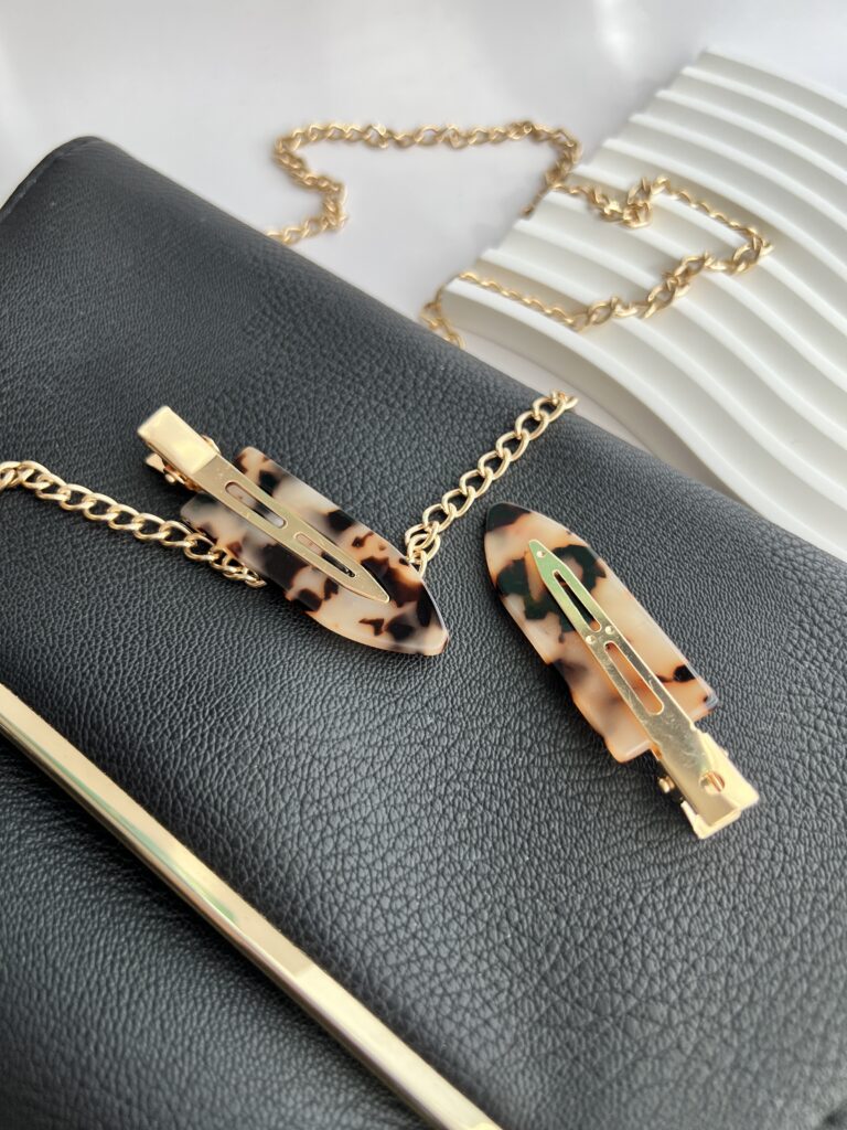 Tigrinių raštų makiažo plaukų segtukai padėti ant juodos delninukės