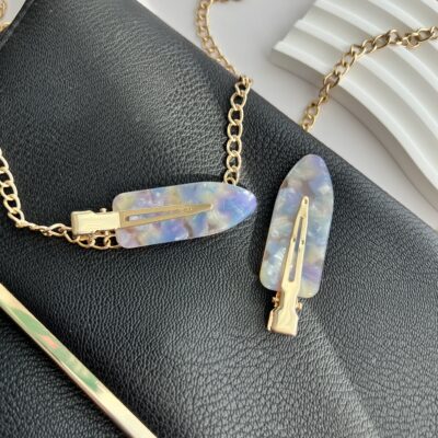 Violetinių ir melsvų spalvų makiažo plaukų segtukai padėti ant juodos delninukės