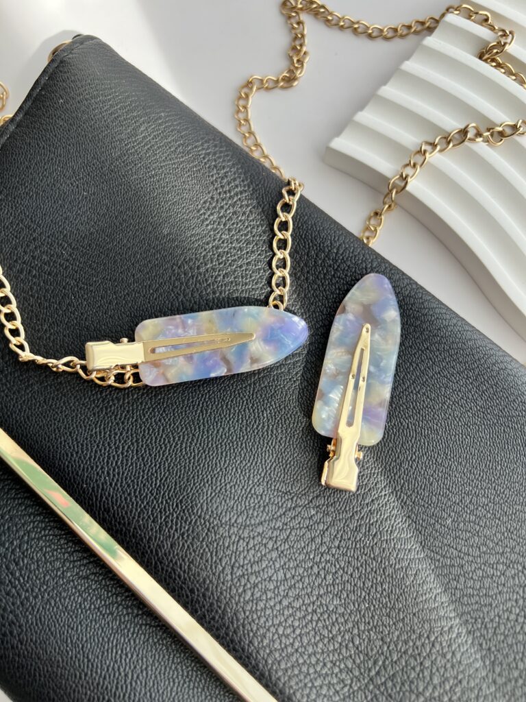 Violetinių ir melsvų spalvų makiažo plaukų segtukai padėti ant juodos delninukės