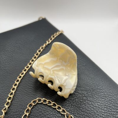 Šviesių kreminių spalvų plaukų segtukas žnyplės padėtas ant juodos delninukės