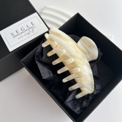 Šviesių spalvų (gelsvos ir baltos) plaukų segtukas žnyplės juodoje dėžutėje.