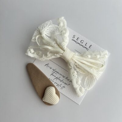 Kreminės spalvos kaspinas mergaitėms ir rusvos spalvos plaukų segtukas su širdele mergaitėms baltame fone