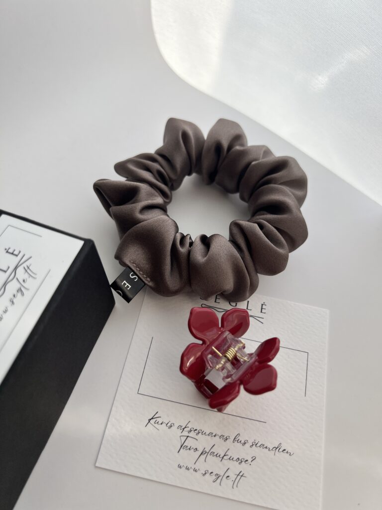 baltame fone šalia juodos dėžutės šilkinė plaukų gumytė pilkai rusvos spalvos ir raudonas gėlės formos plaukų segtukas