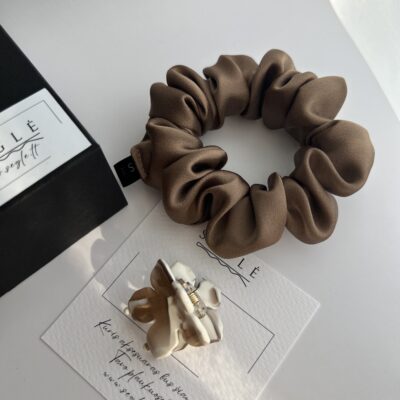 Plaukų aksesuarų rinkinys, kuriame yra šokoladinės spalvos šilkinė plaukų gumytė ir gėlės formos baltai rusvas plaukų segtukas