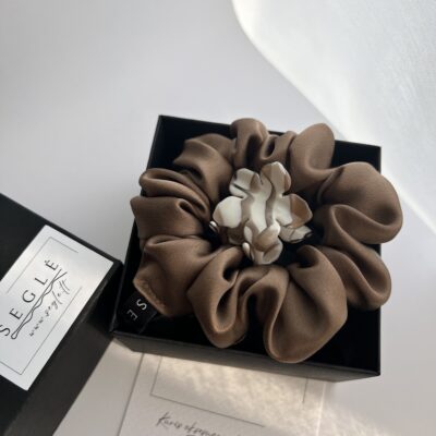 Juodoje dėžutėje šokoladinės spalvos šilkinė plaukų gumytė ir gėlės formos nedidelis plaukų segtukas