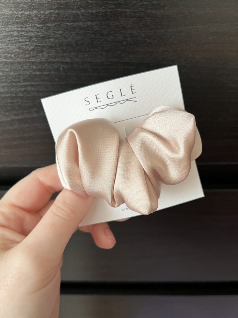 Plaukų segtukas šviesios pudros spalvos pagamintas iš dirbtinio šilko. Segtukas baltoje kortelėje juodame fone