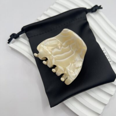 Nedidelis plaukų segtukas žnyplės, kurio paviršius atrodo lyg išlietas baltas šokoladas. Segtukas baltame fone ant juodo maišelio