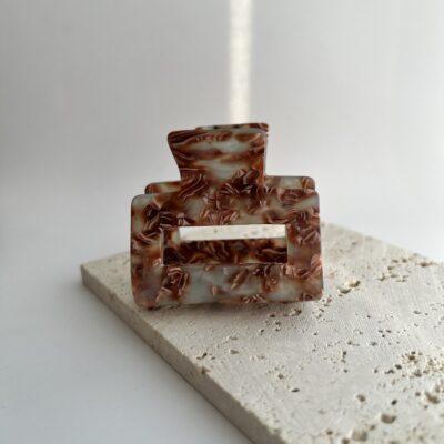 Pilkai melsvos spalvos su rudais ornamentais plaukų segtukas žnyplės. Segtukas baltame fone ant rusvo akmeninio padėkliuko