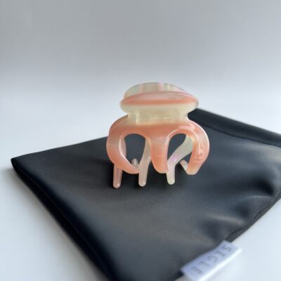 Krabo formos plaukų segtukas žnyplės ant juodo maišelio. Segtukas šviesios perlamutrinės spalvos su rausvais atspalviais