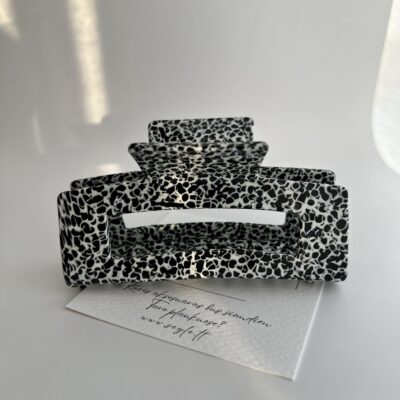 Didelis plaukų segtukas žnyplės baltos spalvos su juodais taškeliais. Segtukas baltame fone