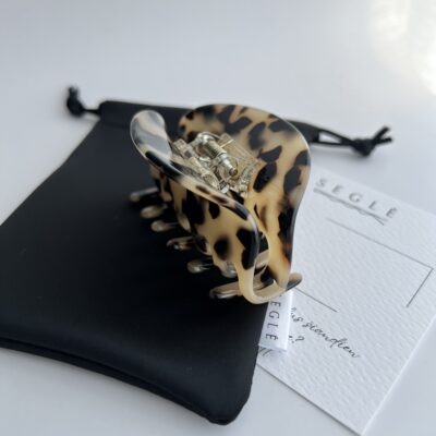 Migdolinės spalvos su juodomis dėmelėmis plaukų segtukas žnyplės baltame fone ant juodo maišelio