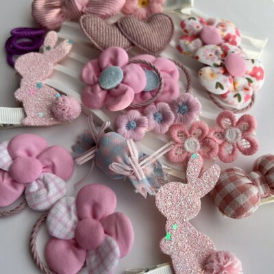 Daug rausvos spalvos plaukų segtukų ir gumyčių mergaitėms baltame fone