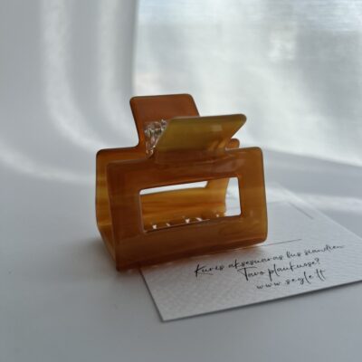 Šviesios kavos spalvos plaukų segtukas žnyplės baltame fone. Segtukas kvadratinės formos