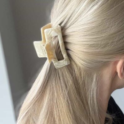 Susegta dalis plaukų su plaukų segtuku žnyplėmis, kurio paviršius atrodo lyg išlieto balto šokolado