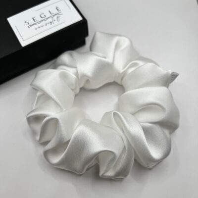 baltos spalvos šilkinė plaukų gumytė baltame fone šalia juodos dėžutės