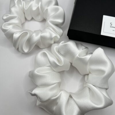 Dviejų dydžių baltos šilkinės plaukų gumytės baltame fone šalia juodos dėžutės