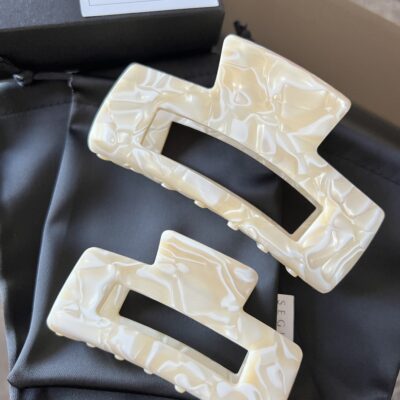 Dviejų dydžių plaukų segtukai, kurių paviršius atrodo lyg išlietas baltasis šokoladas