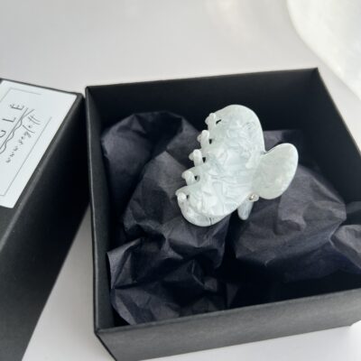 Nedidelis pilkai melsvos spalvos su baltais raštais plaukų segtukas žnyplės juodoje dėžutėje