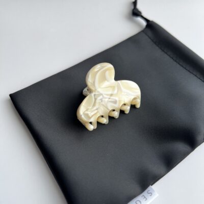 Nedidelis plaukų segtukas žnyplės padėtas ant juodo maišelio. segtuko paviršius atrodo lyg išlietas baltas šokoladas