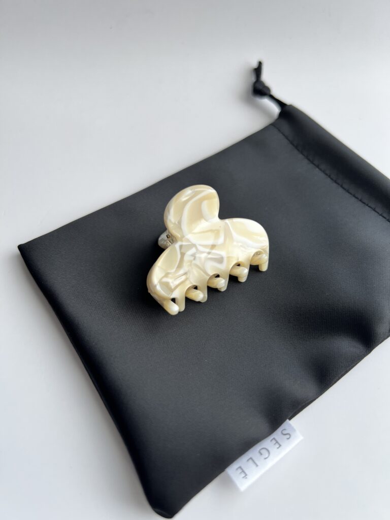 Nedidelis plaukų segtukas žnyplės padėtas ant juodo maišelio. segtuko paviršius atrodo lyg išlietas baltas šokoladas