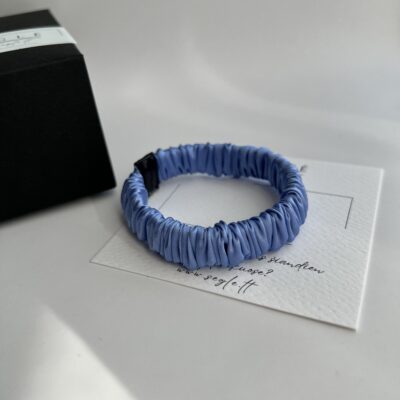 Siaura - mini, šviesiai mėlynos spalvos šilkinė plaukų gumytė baltame fone, šalia juodos dėžutės