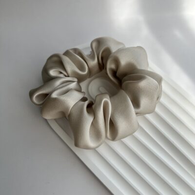 Perlo spalvos šilkinė plaukų gumytė ant balto padėkliuko baltame fone