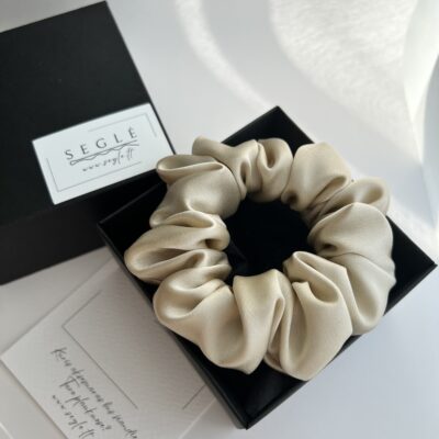 Šampaninės spalvos šilkinė plaukų gumytė juodoje dėžutėje. Dėžutė baltame fone