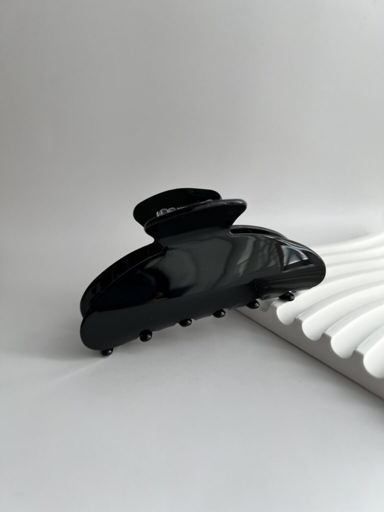 Juodos spalvos plaukų segtukas baltame fone šalia balto padėkliuko