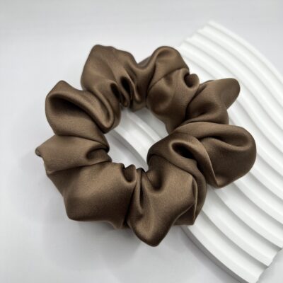 Rudos, šokoladinės spalvos didesnė šilkinė plaukų gumytė baltame fone ant balto banguoto akmeninio padėkliuko