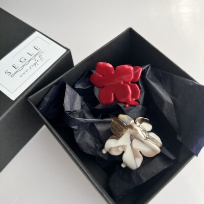 Du nedideli gėlės formos plaukų segtukai juodoje dėžutėje. Viena gėlė raudonos spalvos, kita balta su rudais raštais