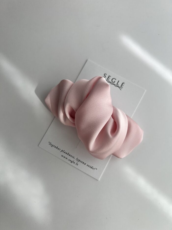 Baby pink spalvos plaukų segtukas. Jo paviršius pagamintas iš poliesterio audinio, užsegimas metalinis.