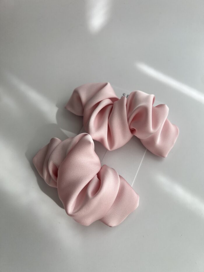 Baby pink spalvos plaukų segtukai, kurie savo dizainu panašūs į kruasanus. Paviršius pagamintas iš poliesterio audinio, užsegimas metalinis.