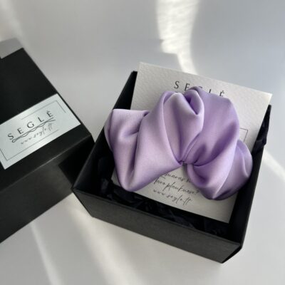 Šviesios violetinės spalvos plaukų segtukas juodoje dėžutėje. Segtukas pagamintas iš dirbtinio šilko