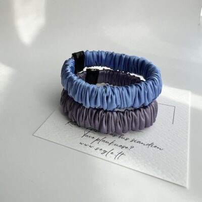 Dvi siauros šilkinės plaukų gumytės baltame fone. Gumytės šviesios levandų ir melsvos spalvos