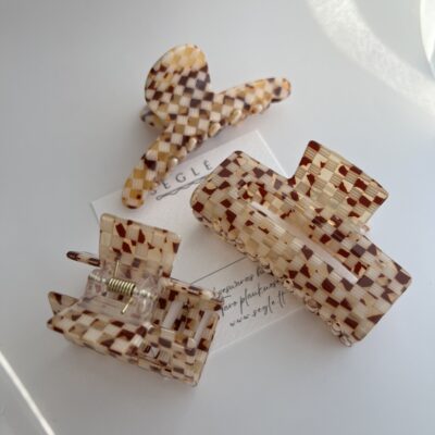 Trys skirtingų formų ir dydžių plaukų segtukai, kurių paviršius atrodo lyg smulki langelių mozaika. Langeliai šviesių rudų spalvų