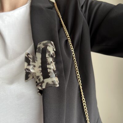 Plaukų segtukas užsegtas ant juodo švarko. Segtukas kreminės spalvos su juodomis dėmelėmis