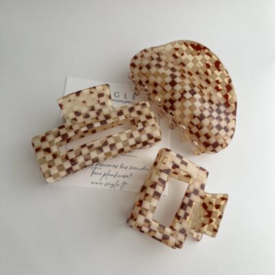 Trijų skirtingų dydžių plaukų segtukai žnyplės. Segtukų paviršius atrodo lyg smulkių langelių mozaika