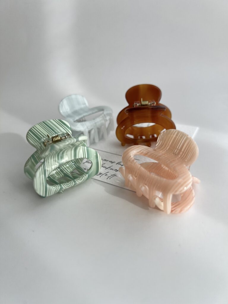 Nedideli plaukų segtukai. Segtukai keturių skirtingų spalvų: rausvas, žalias, pilkas ir rudas. Segtukai baltame fone