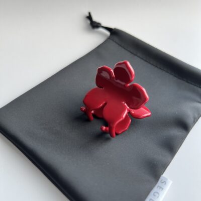 Raudonos spalvos gėlės formos plaukų segtukas padėtas ant juodo maišelio