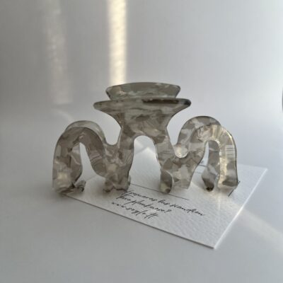 Bangelės formos plaukų segtukas baltame fone. Segtukas pilkos ir baltos spalvos.