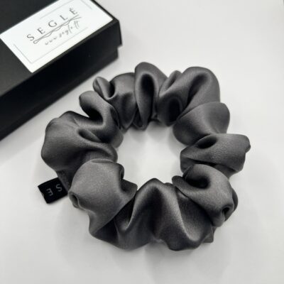 Natūralaus šilko klasikinės pilkos šilkinė plaukų gumytė baltame fone šalia juodos dėžutės