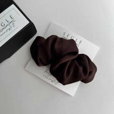 tamsaus šokolado spalvos plaukų segtukas pagamintas iš poliesterio audinio. Segtukas baltame fone šalia juodos dėžutės