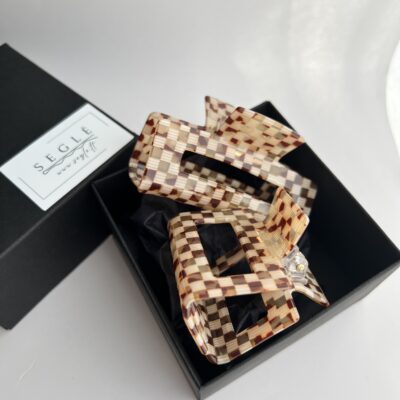 Du plaukų segtukai, kurių paviršius atrodo lyg smulkių langelių mozaika juodoje dėžutėje