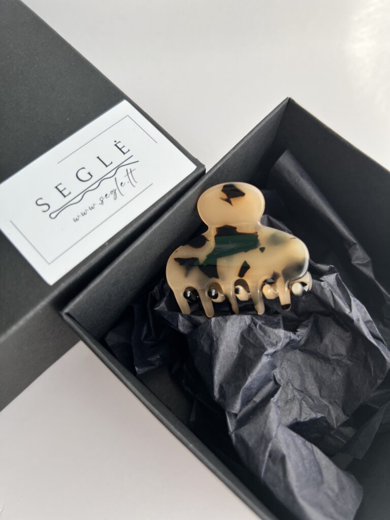 Nedidelis migdolinės spalvos su juodomis dėmelėmis plaukų segtukas žnyplės juodoje dėžutėje