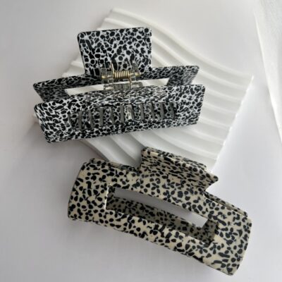 Du dideli plaukų segtukai žnyplės su juodais taškeliais. Vienas segtukas kreminės spalvos, o kitas baltas. Segtukai baltame fone ant akmeninio padėkliuko