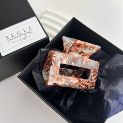 Kvadratinis plaukų segtukas žnyplės juodoje dėžutėje. Segtukas pilkai melsvos spalvos su rudais ornamentais