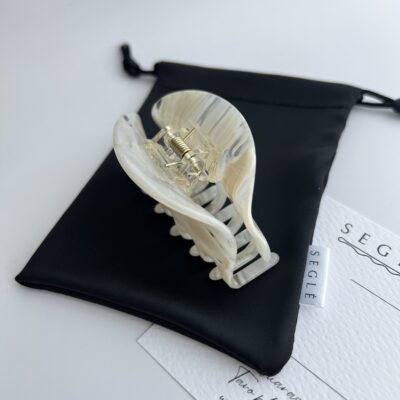 Kriauklės formos milky spalvos plaukų segtukas žnyplės ant juodo maišelio baltame fone