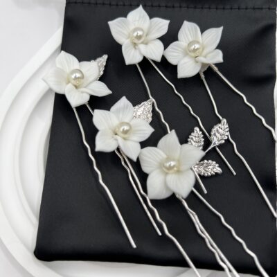 Metaliniai sidabro spalvos plaukų smeigtukai kuodui su baltomis gėlėmis. Smeigtukai ant juodo maišelio